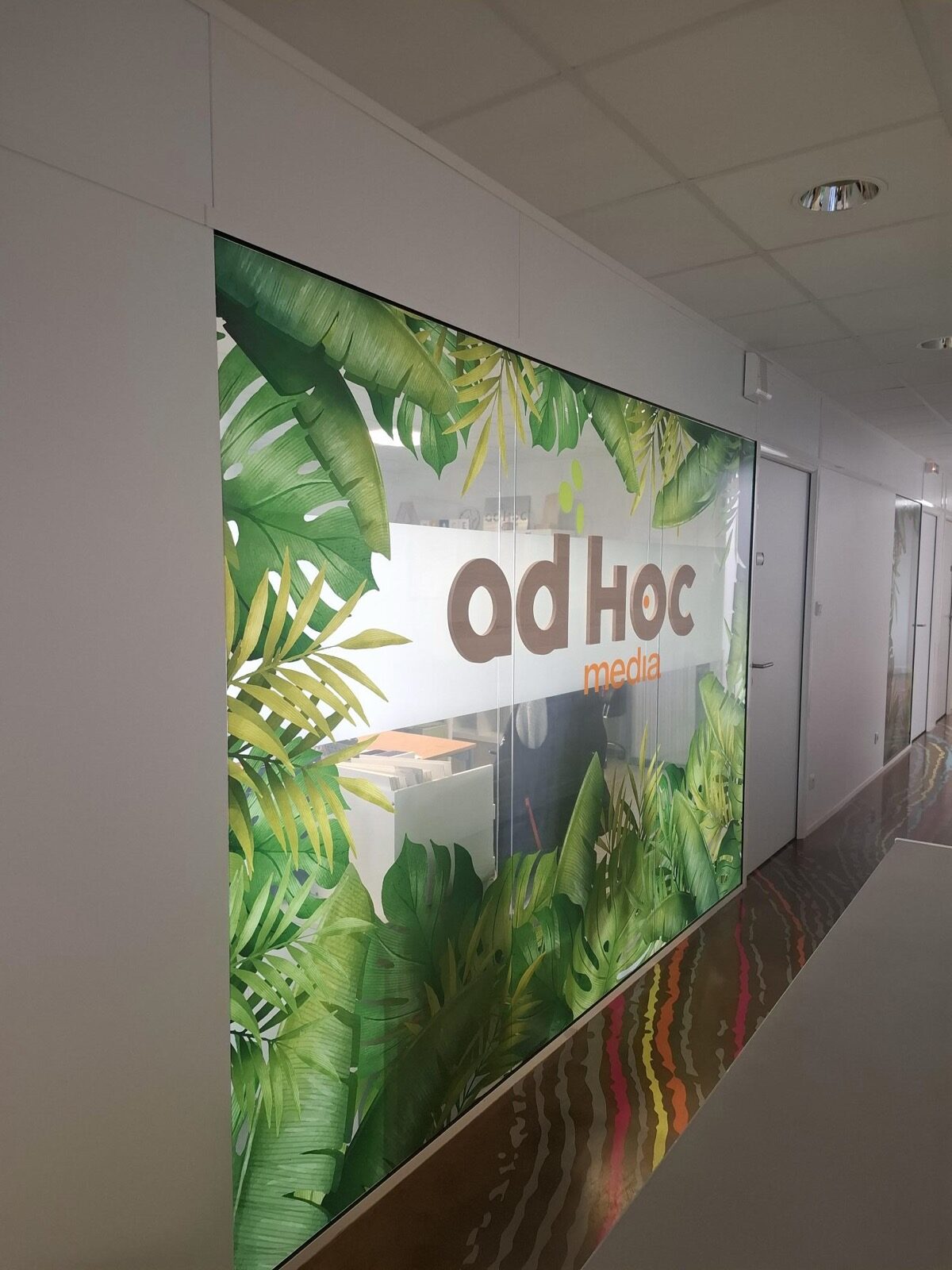 Vitrophanie imprimée à motif végétal et logo Ad'Hoc Media sur une cloison d'accueil de bureau